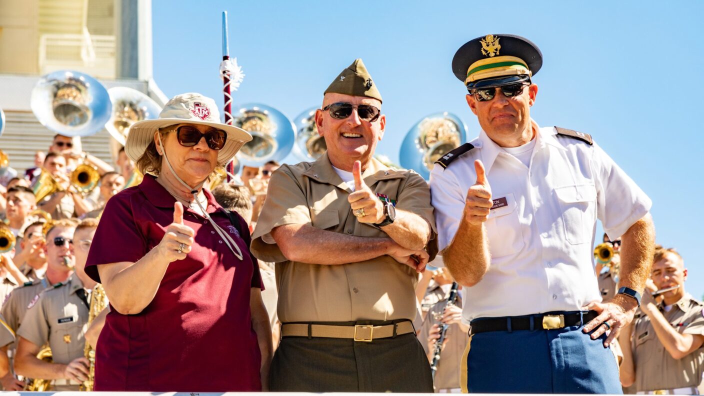 A girl, and two guys in uniform in the crowd at a football game.