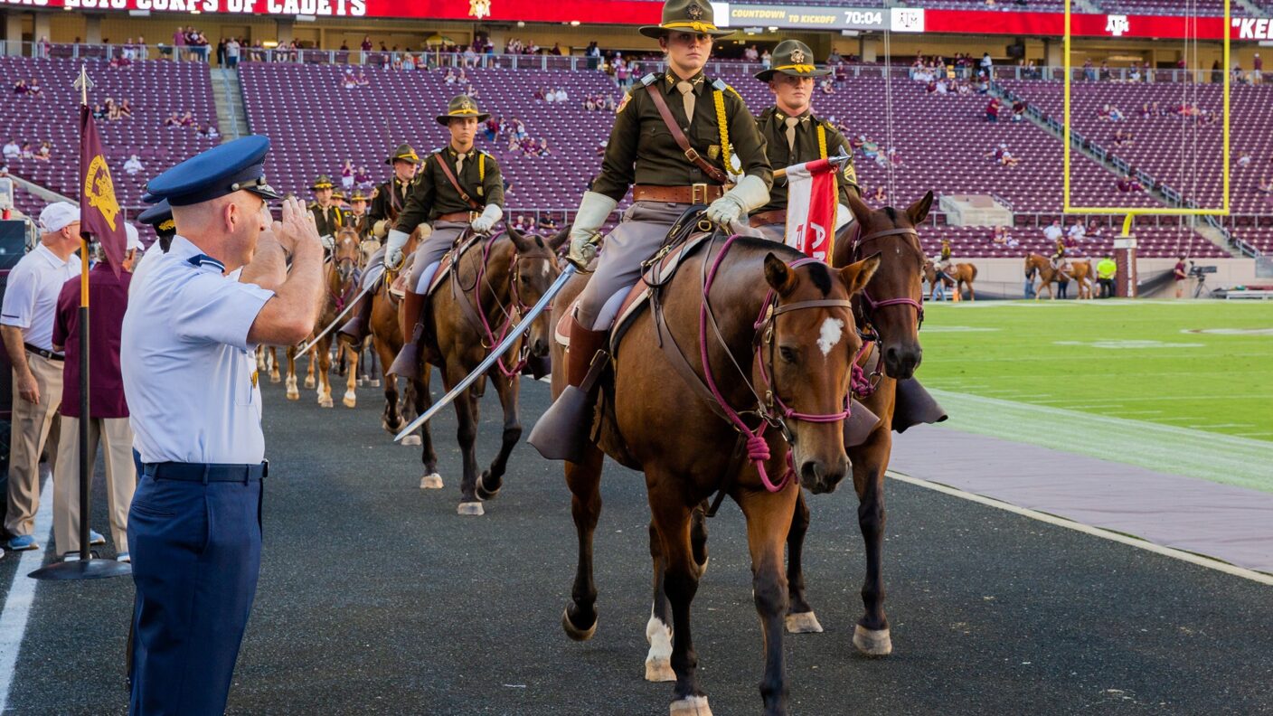 A woman riding on a horse on a football track saluting.
