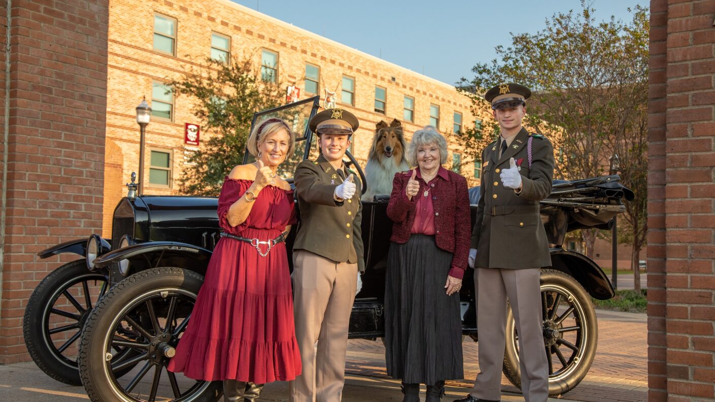 A group of people standing around a Model T car with a rough collie inside the car.