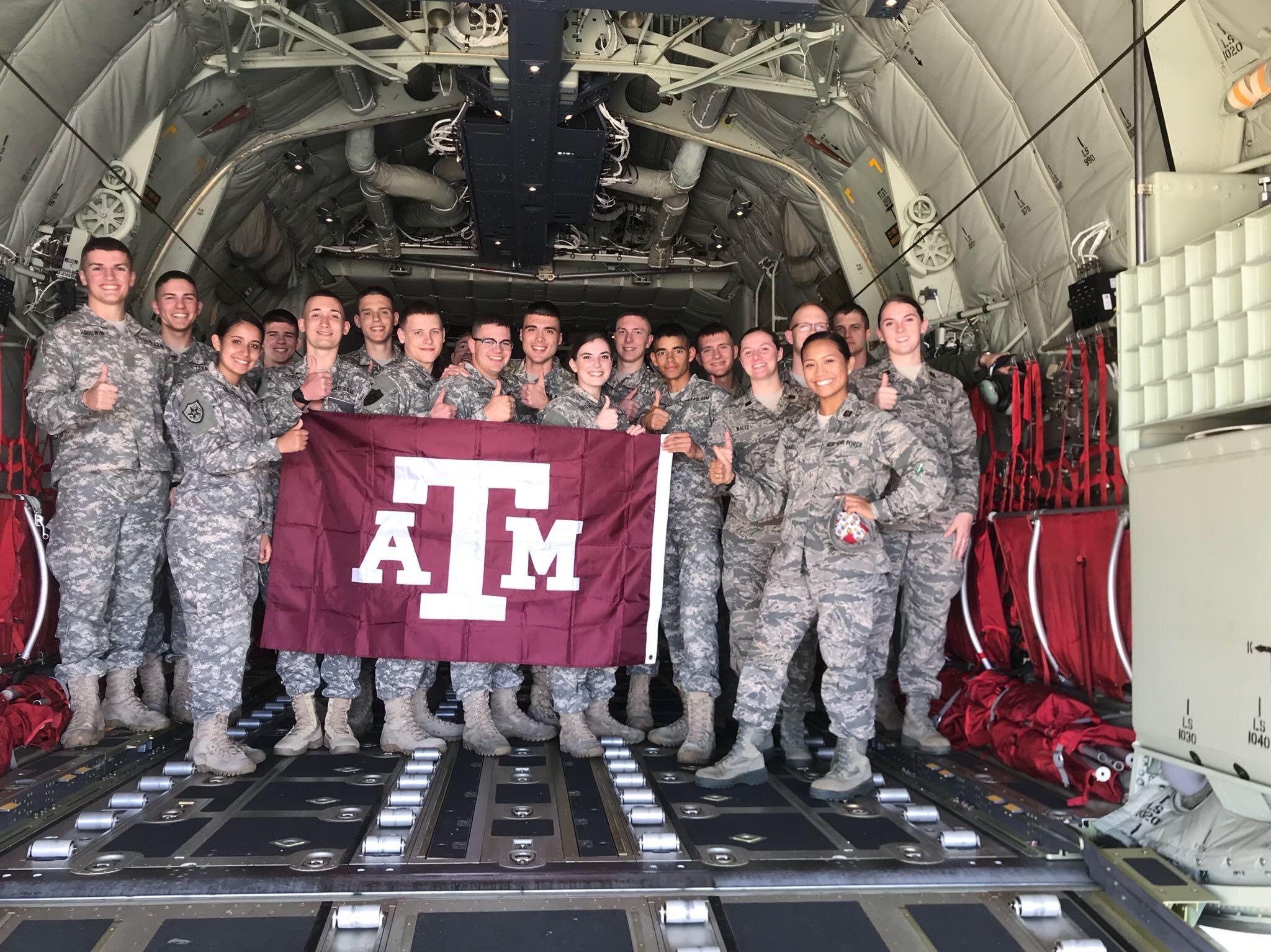 A group of cadets standing in a plane holding an A&M flag