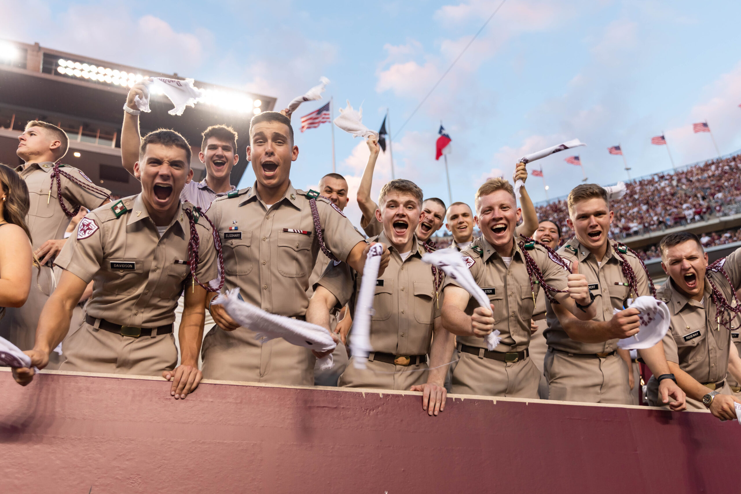 A group of cadets waving towels and cheering in a football stadium.