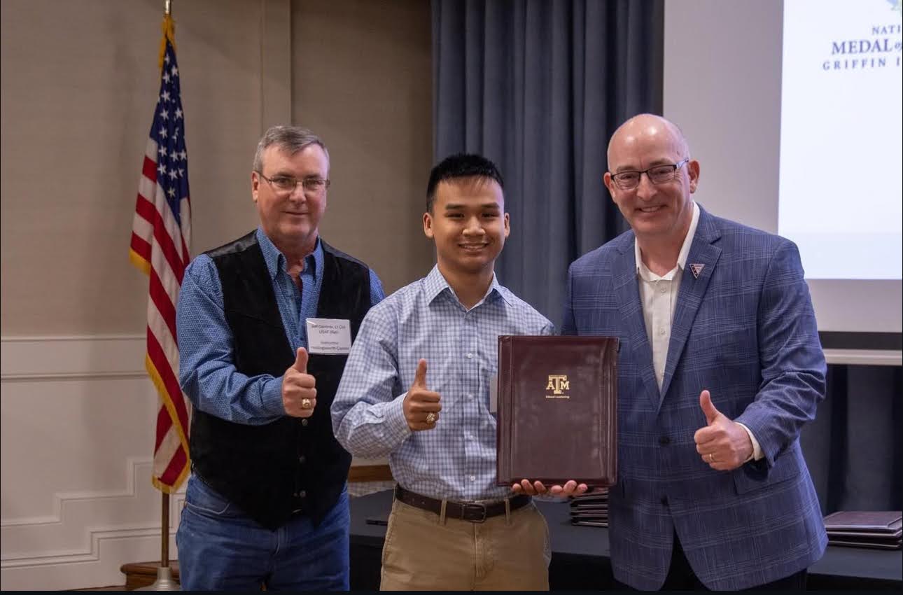 Three guys pose with the guy in the middle holding a plaque.
