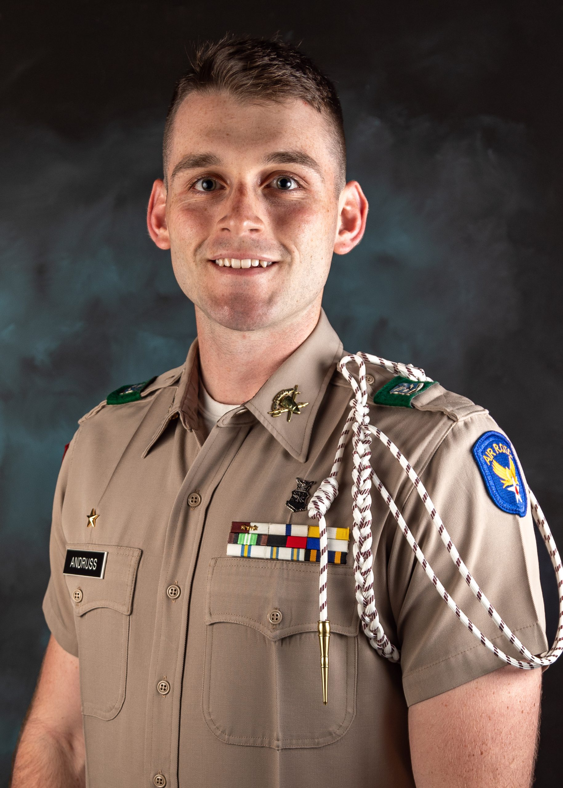 Cadet Joey Andruss '23 smiles in front of a blue studio background