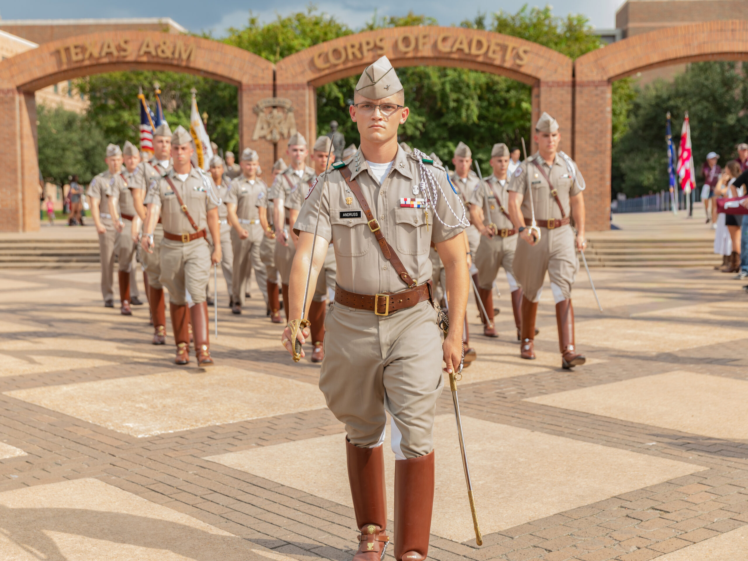 A group of uniformed cadets marching under the Corps arches.